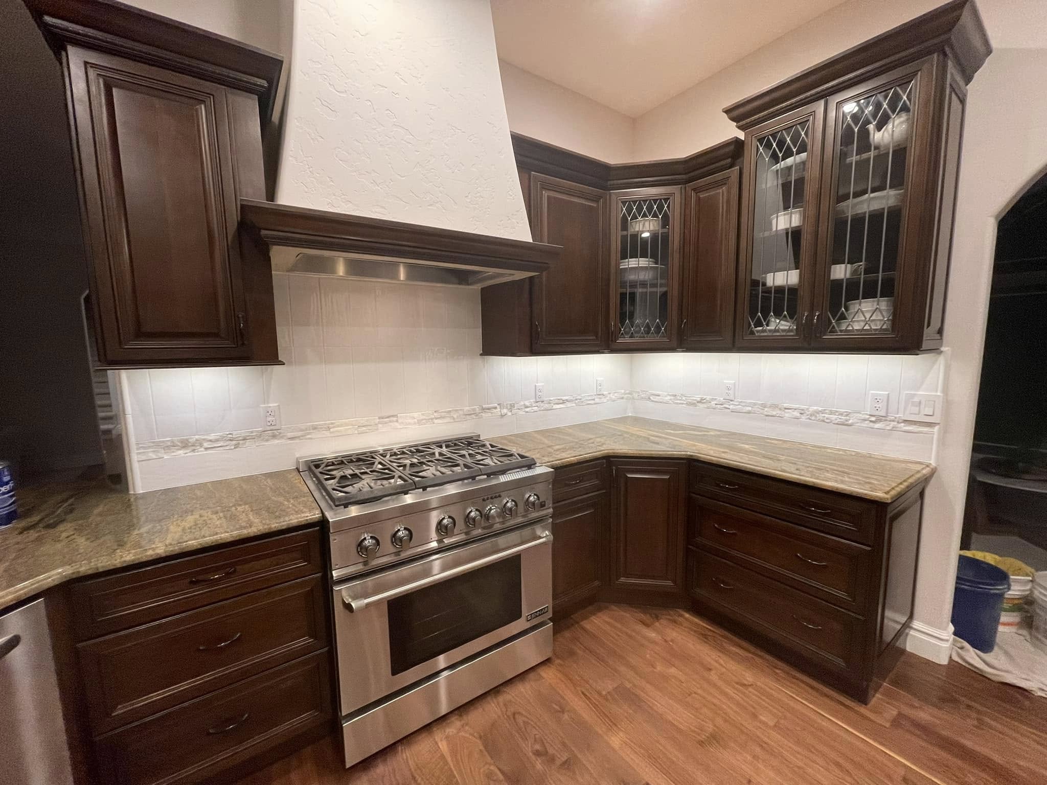 Finished kitchen backsplash with light vertical tile and a decorative accent border beside dark wood cabinetry and a stainless steel range.