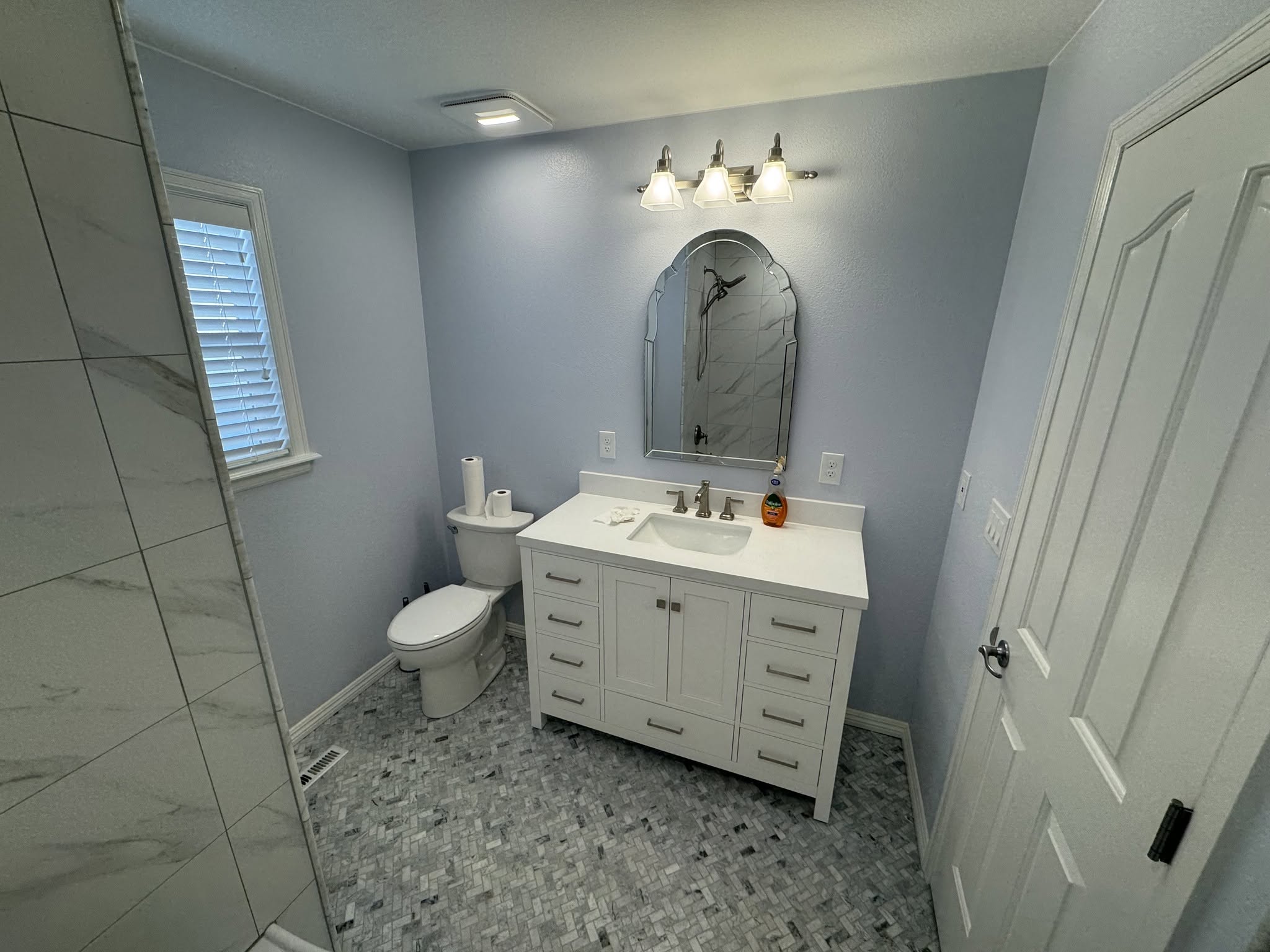 Bathroom with a white vanity, shaped mirror, patterned tile flooring and blue-gray walls.