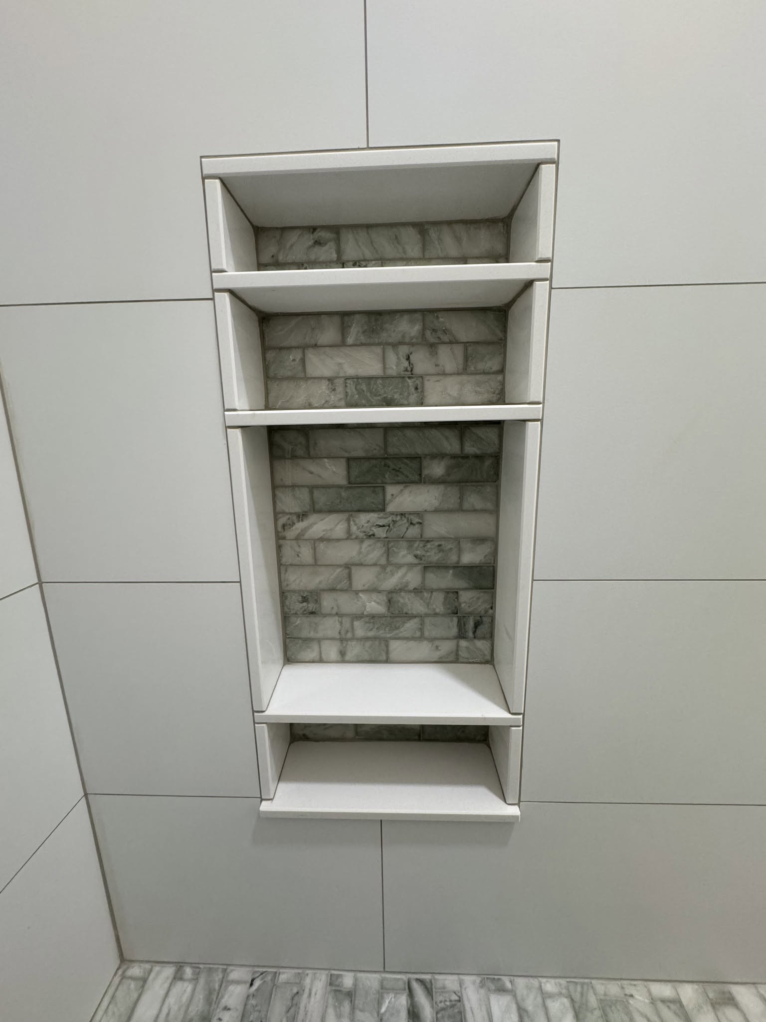 Tall custom shower niche with white shelves and gray patterned tile backing