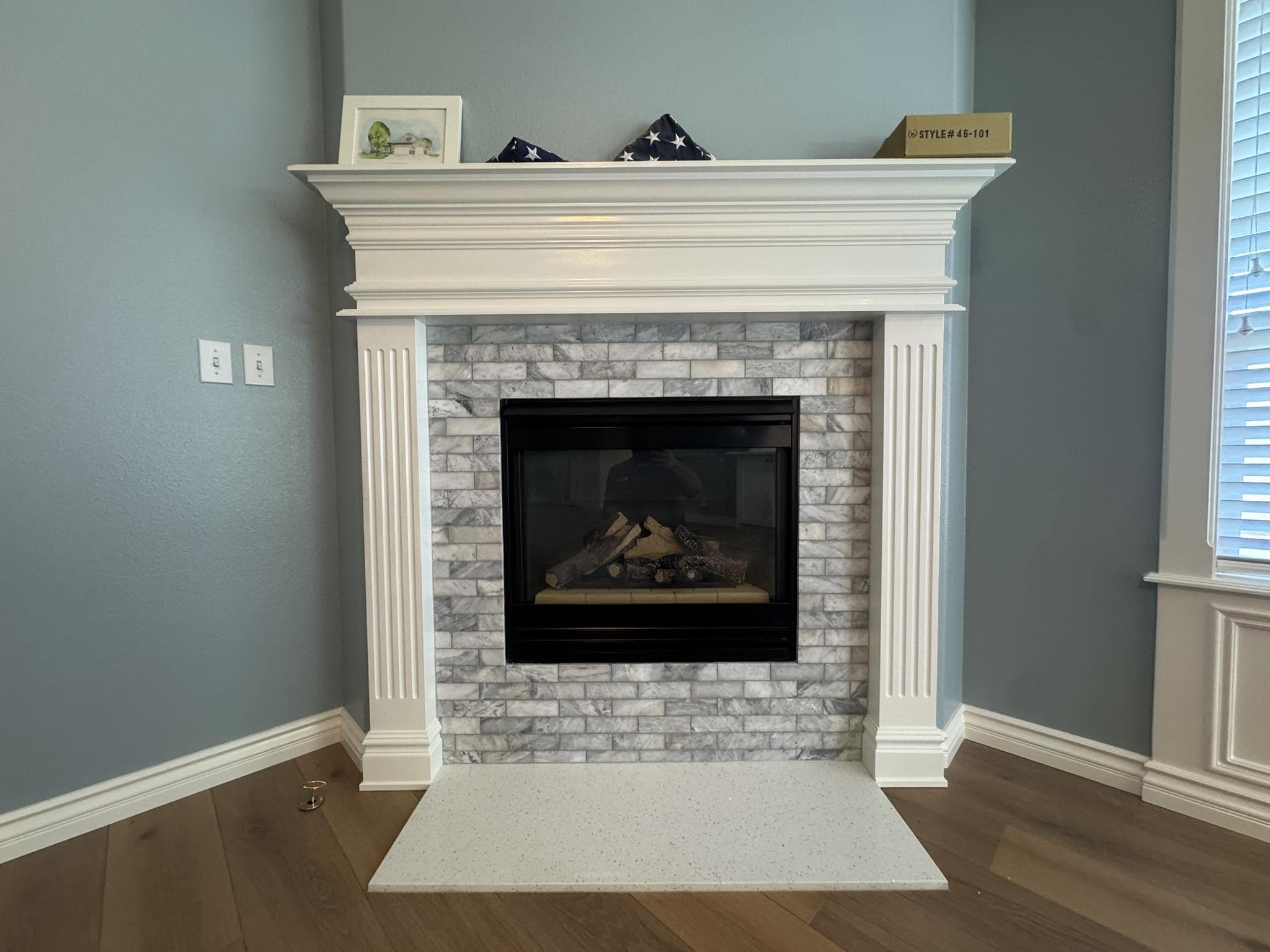 Finished fireplace with blue, gray and tan tile and a white surround. The after photo identified by the owner.