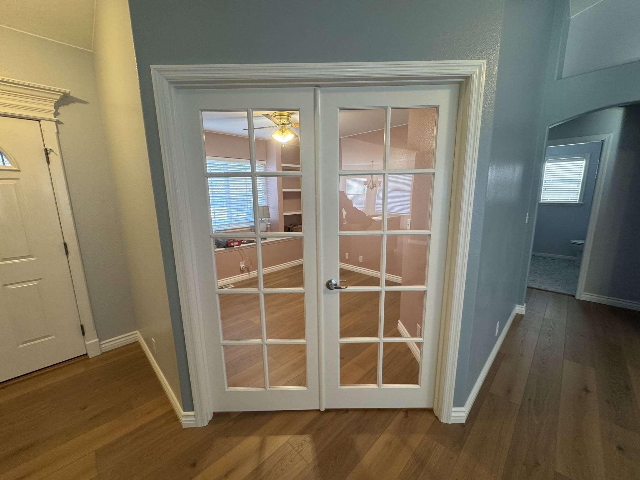 White glass-paneled French doors with layered white trim against blue-gray walls and wood flooring.