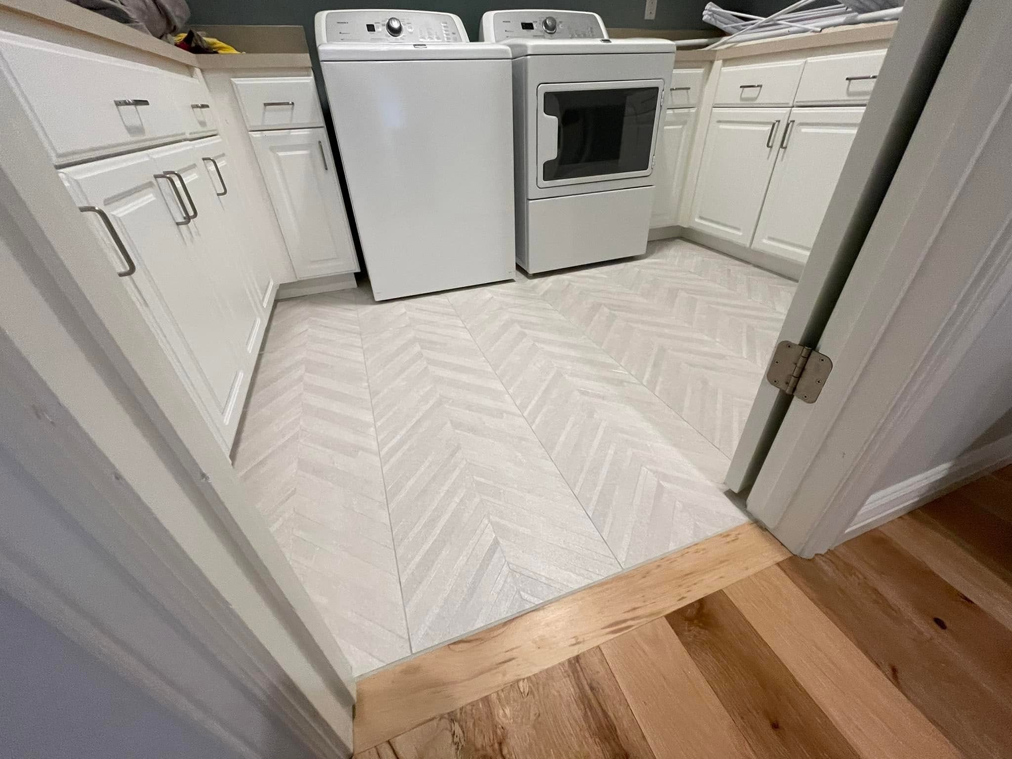 Completed herringbone laundry-room tile floor with white cabinetry, washer and dryer.