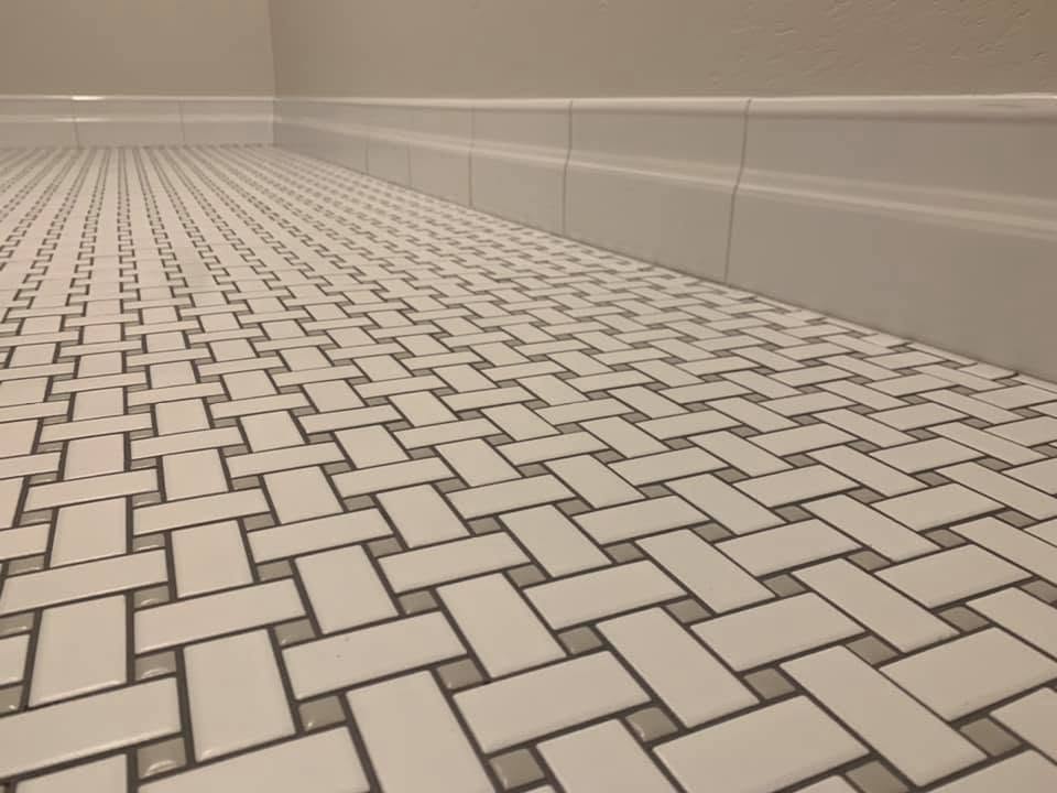 Close view of basketweave laundry floor tile meeting white tile base trim along the wall.