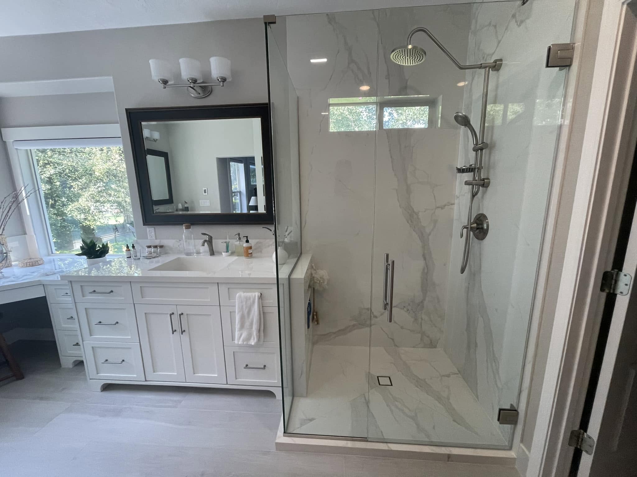 Finished master-bath shower with a frameless glass enclosure, large veined wall tiles, overhead showerhead and handheld shower.