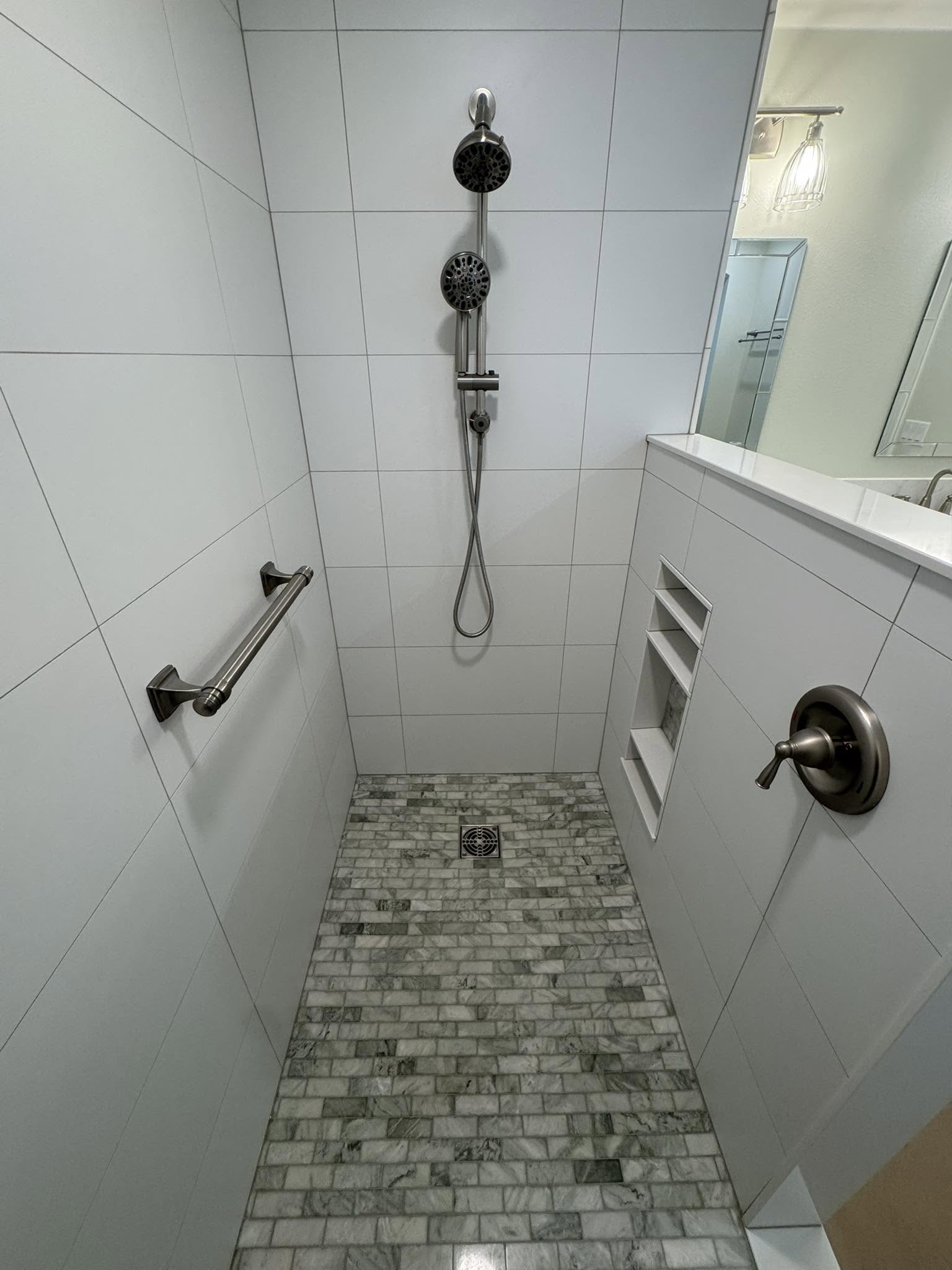 Finished shower with white wall tile, a patterned tile floor, built-in storage and grab bars.